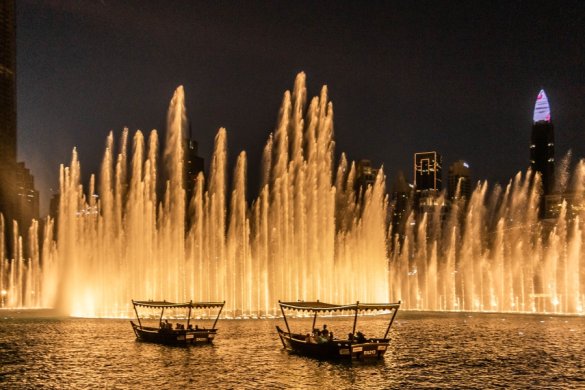 Dubai Fountain show lit up at night with traditional abra boats floating underneath - Dubai Mall Fountain Show Times